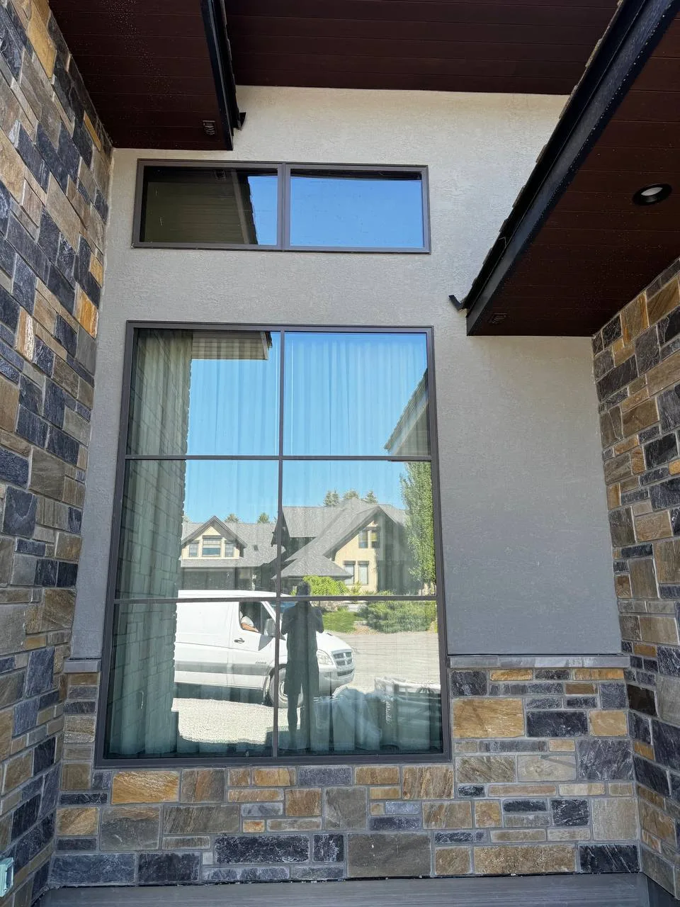 Light grey custom stucco finish seamlessly paired with natural stone veneer and dark wood soffits on a home exterior