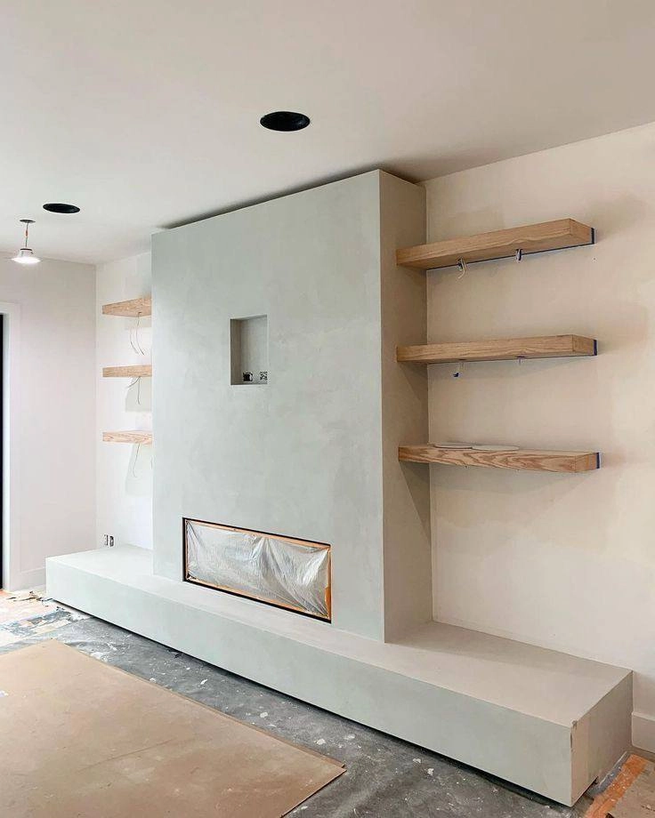 Modern living room featuring a smooth light grey custom stucco finish on a fireplace surround and hearth, accompanied by floating wood shelves