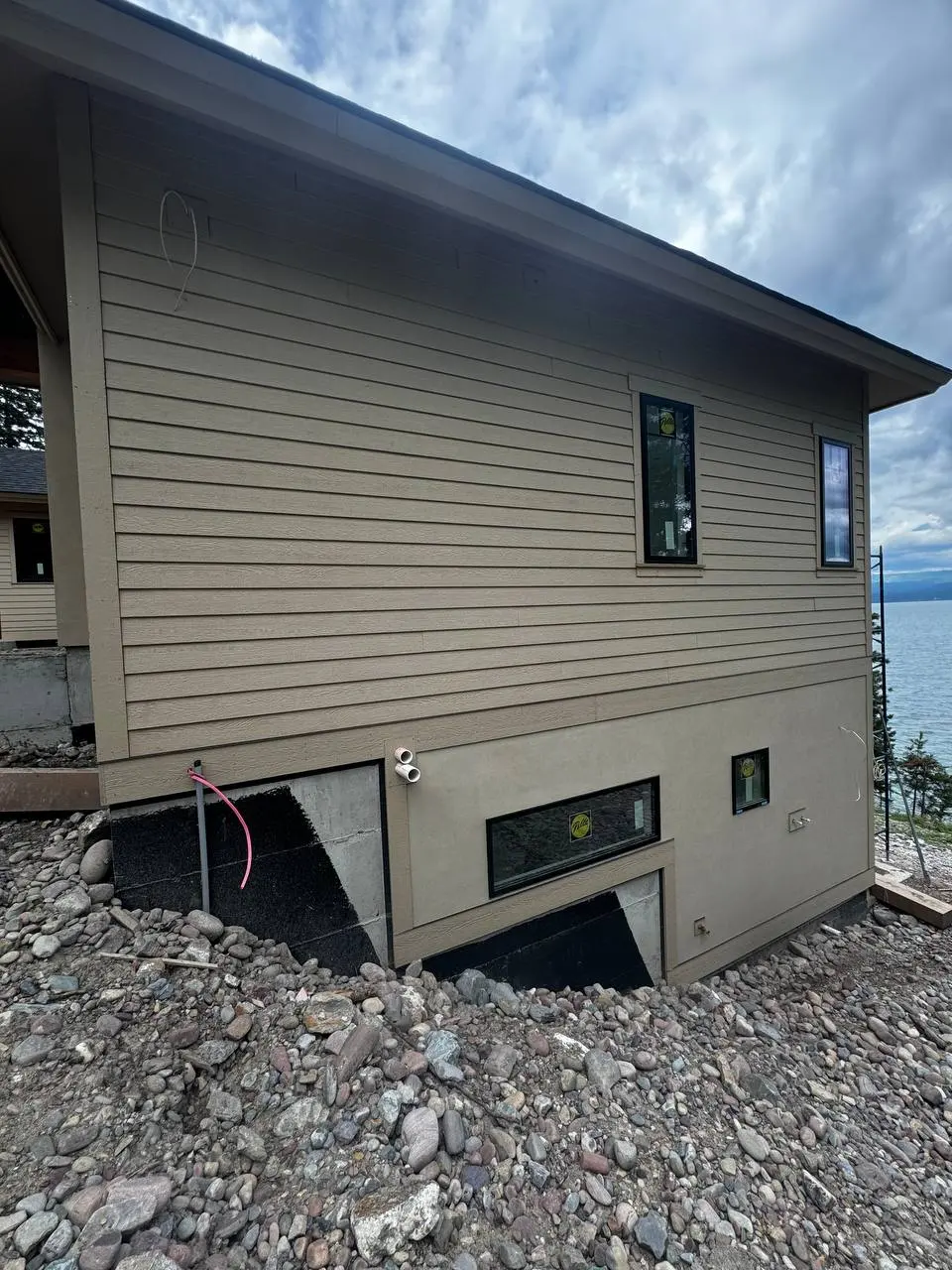 In-progress construction of a lakefront home featuring matching taupe siding and EIFS stucco texture on the lower level by DL Construction