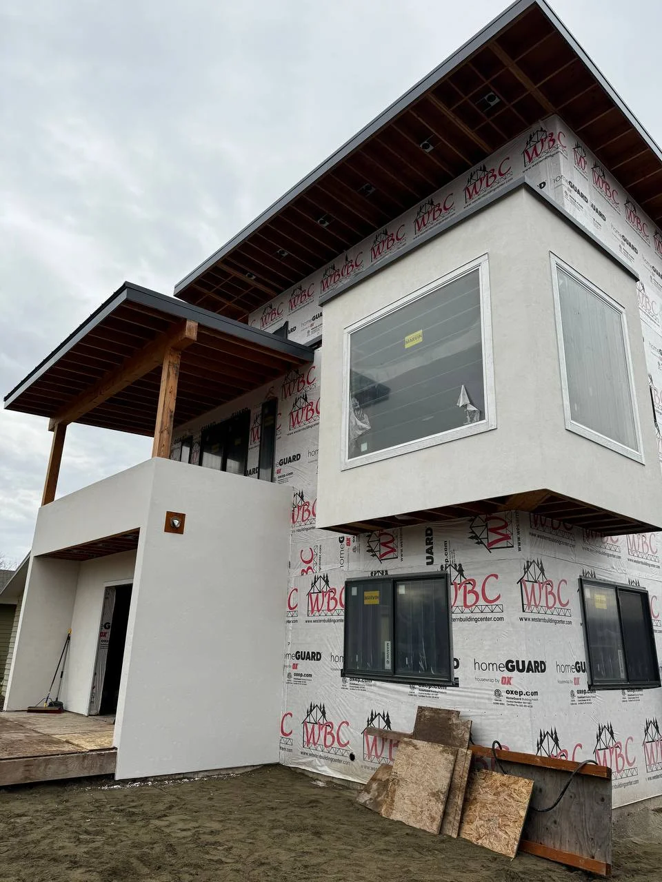 Modern new construction home in Kalispell, MT showing the transition from weather barrier preparation to a flawless smooth white exterior stucco finish