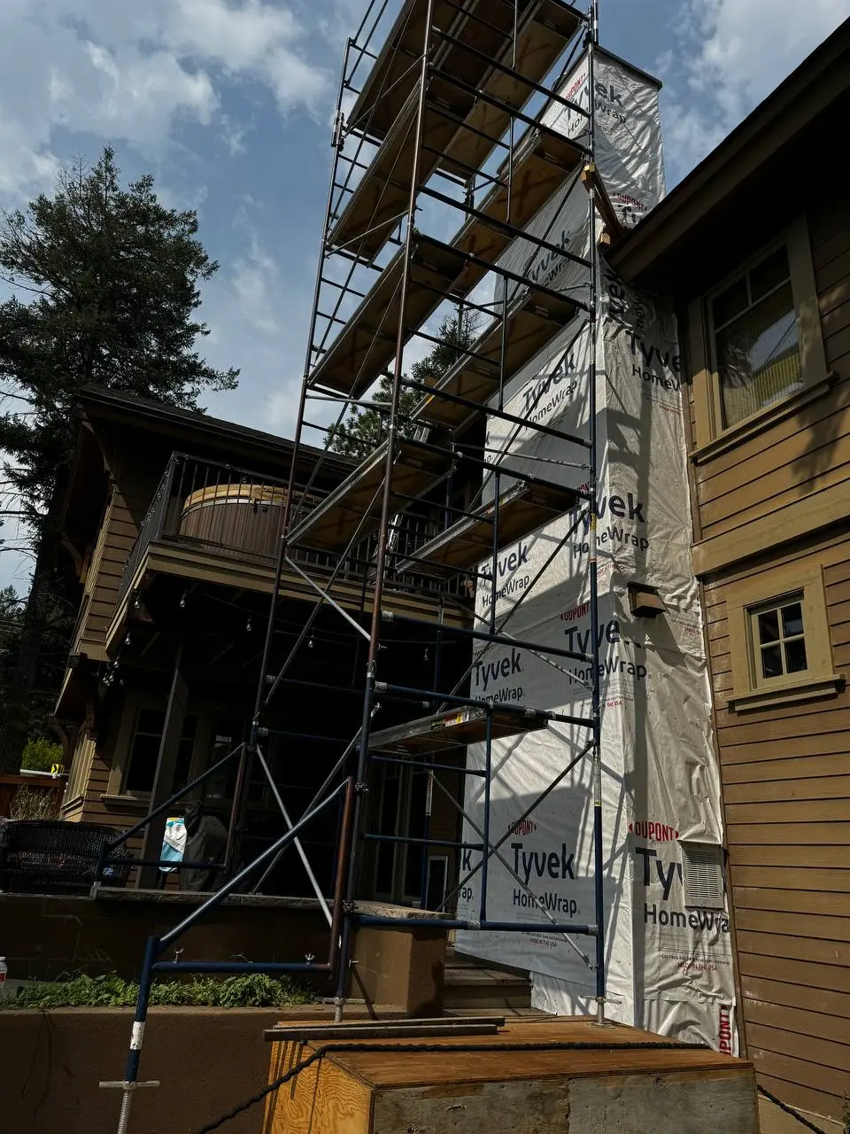 High-reach scaffolding erected around a tall residential chimney structure wrapped in white Tyvek HomeWrap